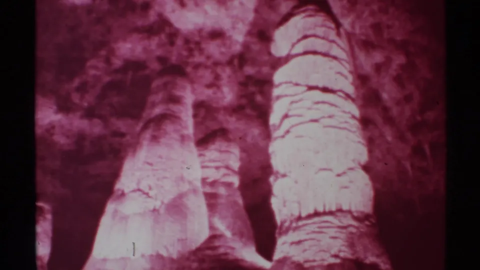 1972 New Mexico 8mm still showing a close, handheld view of layered cave formations in dim magenta-tinted light.