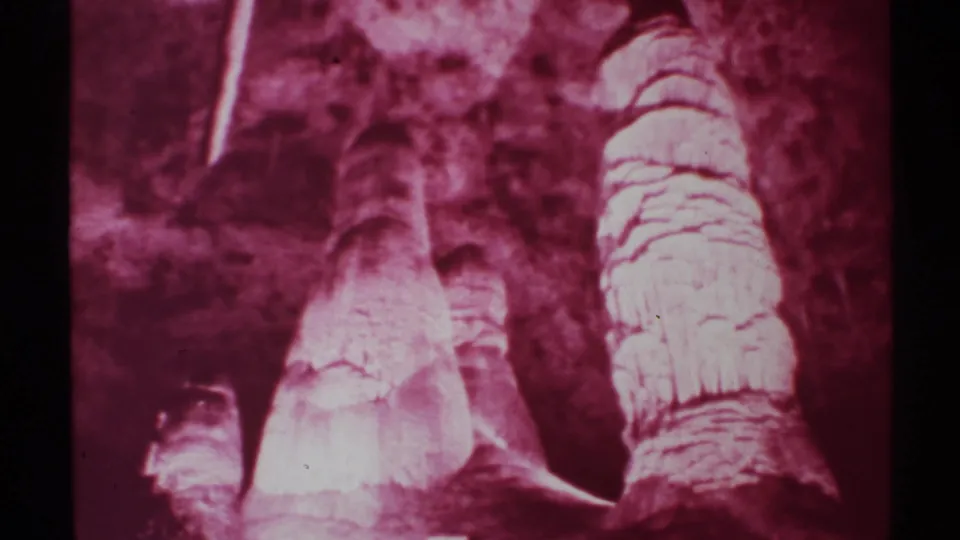 End frame of a 1972 New Mexico cave interior, showing red-lit layered formations, dark recesses, and visible 8mm film texture.