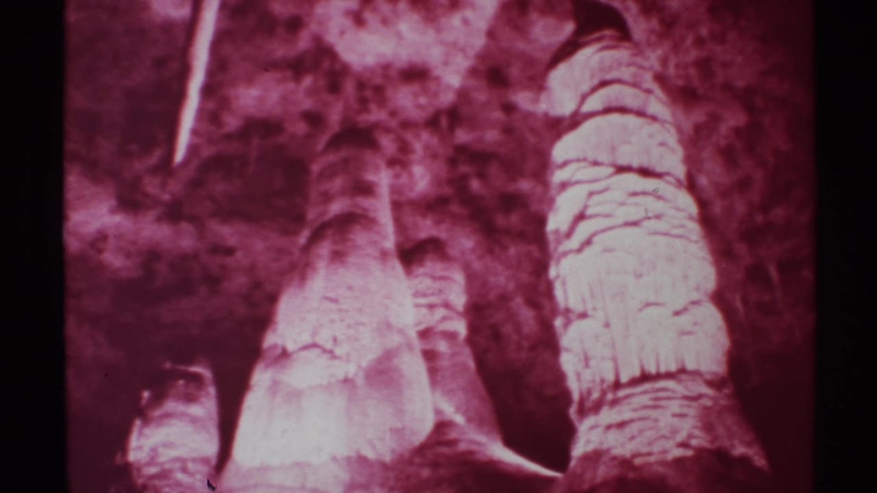 Red-tinted cave formations with stalagmites, stalactites, dark rock walls, and black film borders.