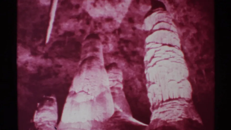 1972 New Mexico 8mm frame showing red-lit stalagmites and stalactites against dark cavern walls, with visible film-frame edges.