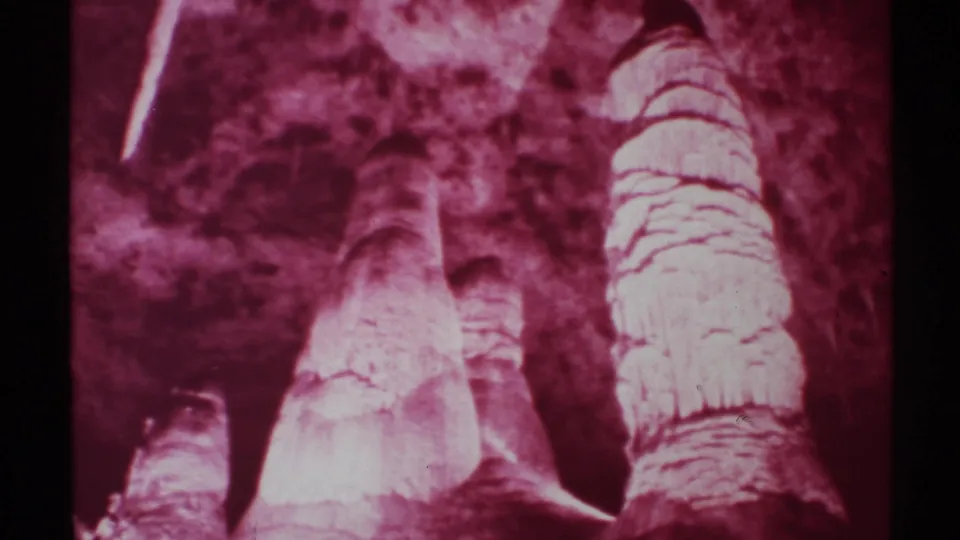 1972 New Mexico 8mm still holding on red-lit cave formations, with layered limestone texture and dark cavern background.