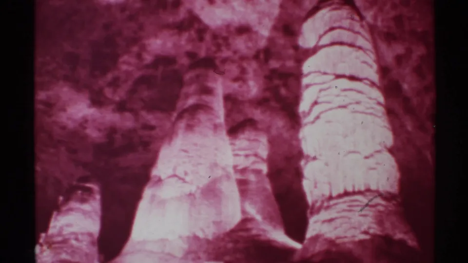 1972 New Mexico 8mm frame of tall cave formations and shadowed gaps, with reflected light and pronounced magenta-purple tint.