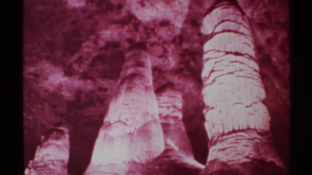 1972 New Mexico 8mm frame showing red-filtered cave formations, including tall pale rock columns against a darker cavern wall.