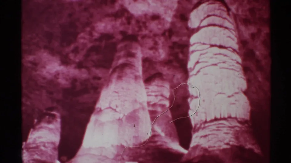 Red-filtered 8mm view of New Mexico cave columns with rough stone surfaces, dark recesses, and light film wear across the frame.
