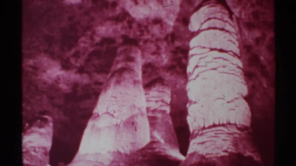 Final 8mm frame showing red-filtered New Mexico cave columns, layered stone bands, shadowed openings, and a soft home-movie exposure.