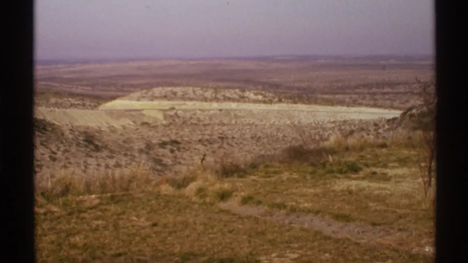 1972 New Mexico home-movie view across an empty arid plain, with scrubby foreground grass, low hills, and faded 8mm color.