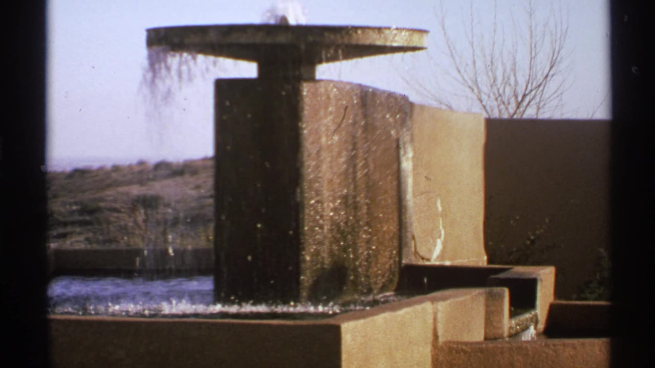 Concrete fountain with water spilling from a circular top into a shallow basin.
