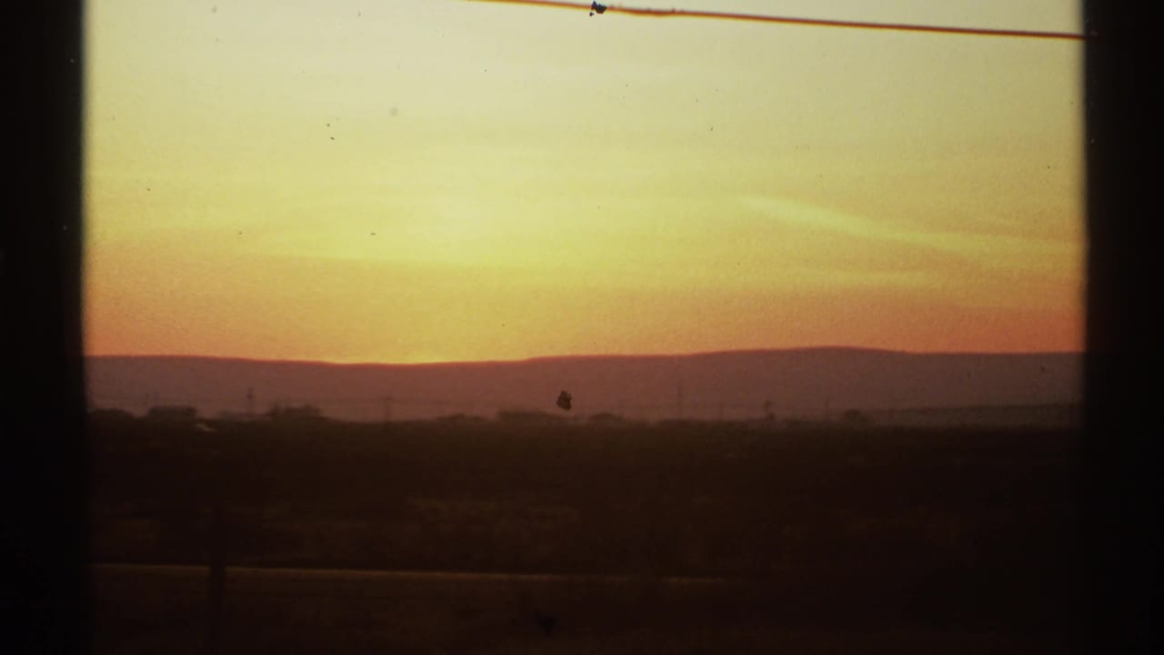 Golden sunset over distant low hills, framed by dark vertical edges.