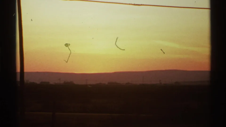 1972 8mm view of a New Mexico horizon at sunset, with amber sky, silhouetted land, and visible film scratches.