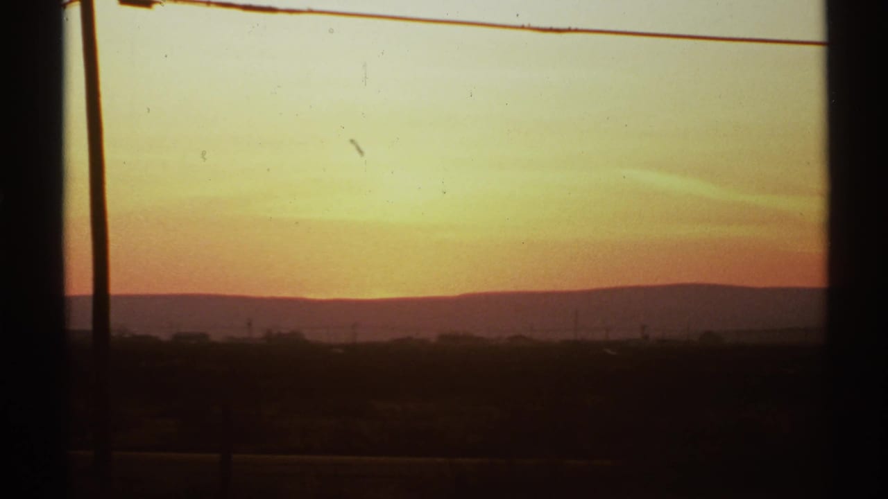 Sunrise over distant hills seen through dark vertical window framing.