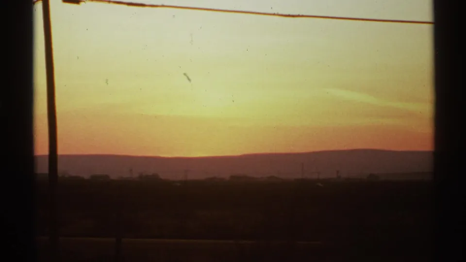 1972 8mm view of a New Mexico sunrise, with orange sky, low hills, open land, and dark window or vehicle framing.