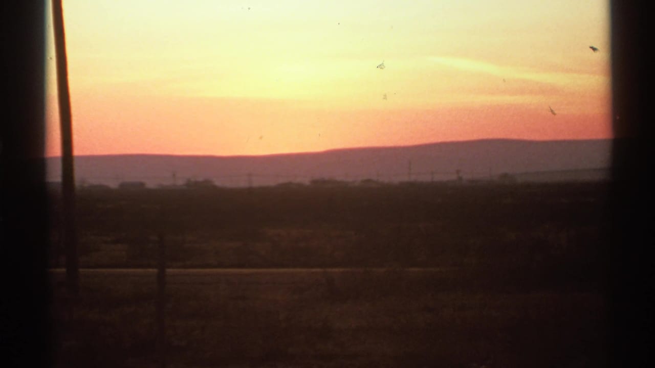 Orange sunset over distant hills seen through dark window frames.
