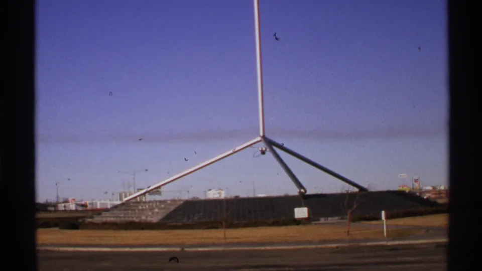 1972 New Mexico home-movie frame showing a silver metal sculpture, low roadside landscape, and clear sky with film dust marks.