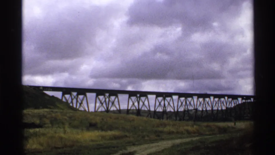Wide 8mm view of a long railway trestle in Valley City, North Dakota, with grassland and heavy clouds.
