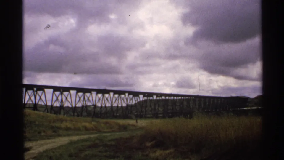 Final 1972 North Dakota frame of the trestle bridge stretching into the distance with grass, roadbed, and dark window edges visible.