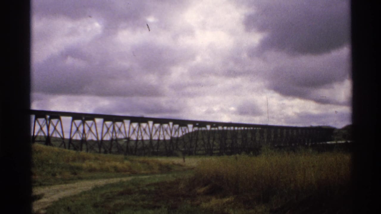 1972 North Dakota 8mm frame showing a long trestle bridge across grassland under a dark, cloud-filled sky.