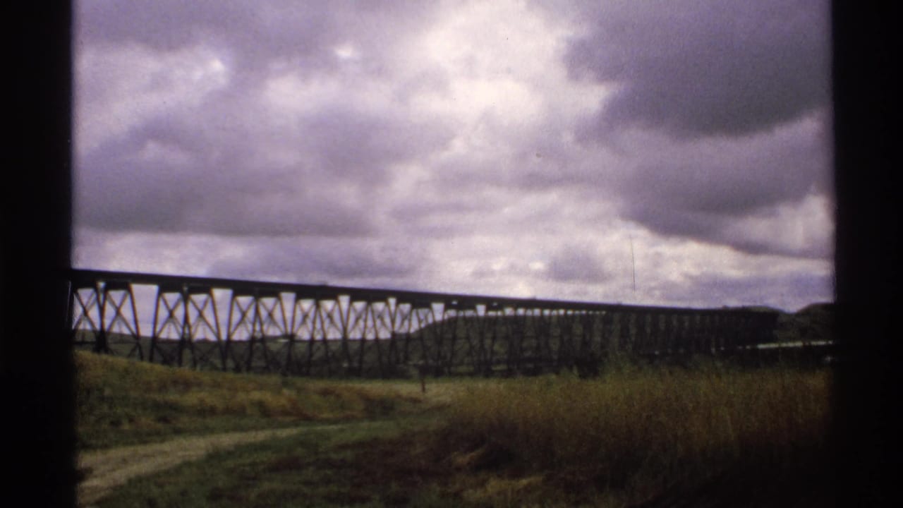 1972 North Dakota home-movie view of a dark trestle bridge, roadside grass, and low stormy clouds.