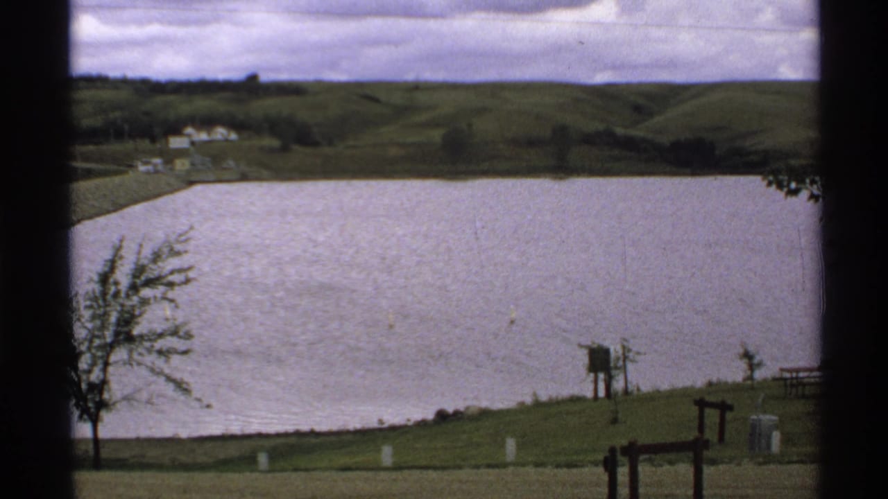 1972 North Dakota home-movie view across Lake Ashtabula Reservoir toward rolling hills and distant buildings.