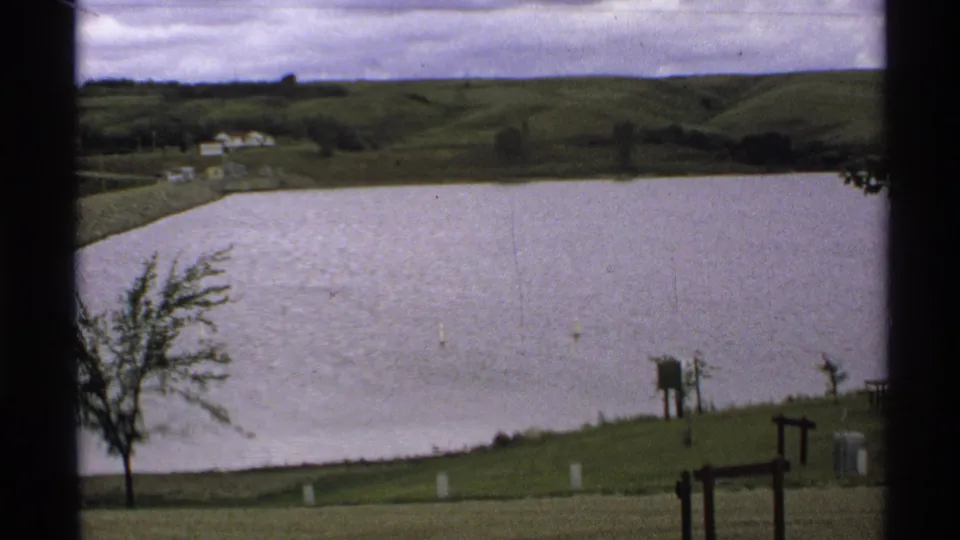 Visitor-shot 8mm frame of Lake Ashtabula Reservoir, showing open water, green hills, and shoreline details in 1972 North Dakota.