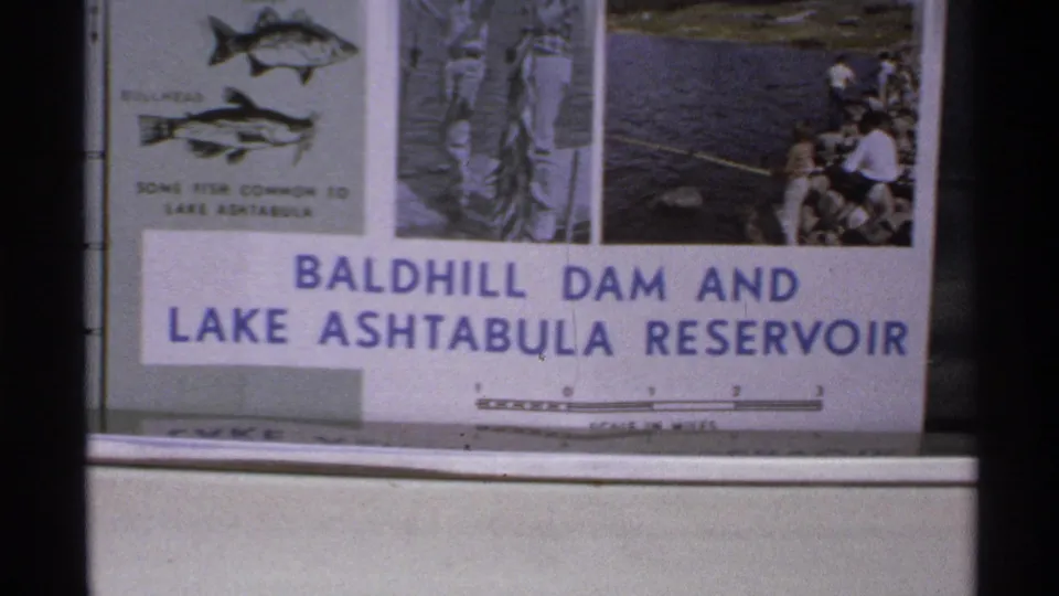 Baldhill Dam and Lake Ashtabula Reservoir sign in North Dakota, with fish illustrations and people visible at the right edge.