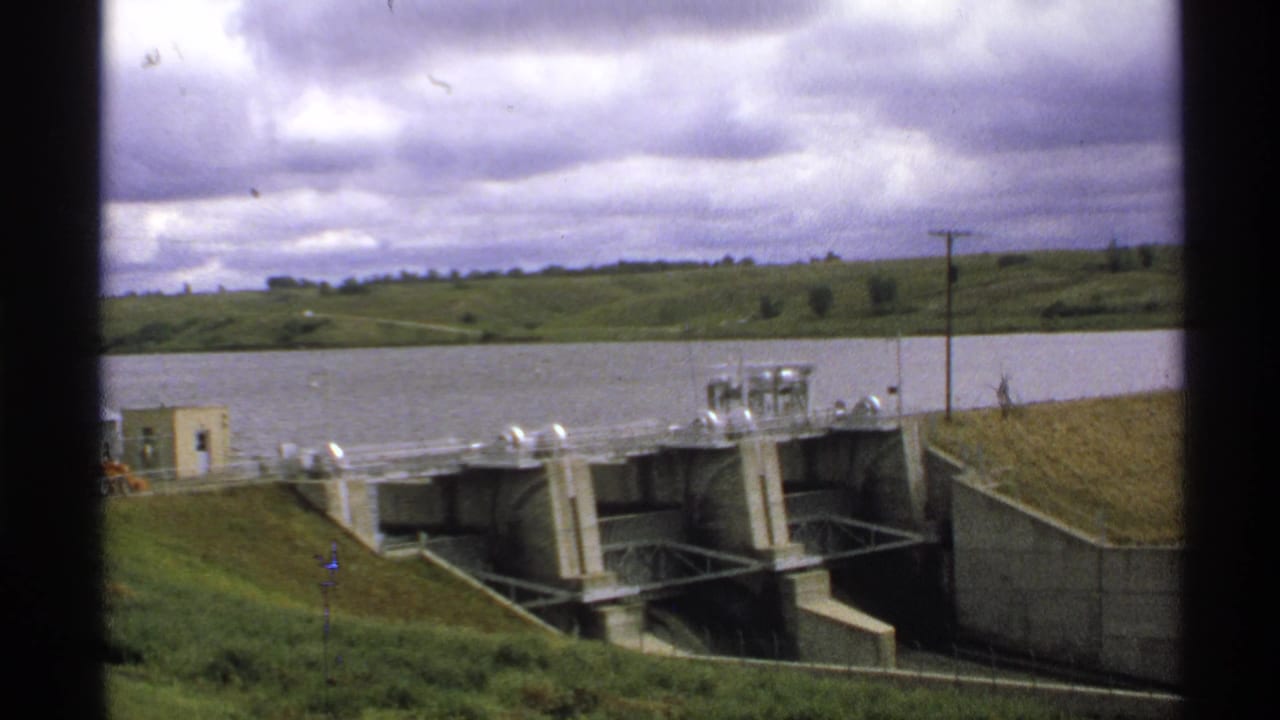 Concrete dam gates beside a reservoir under a cloudy sky.