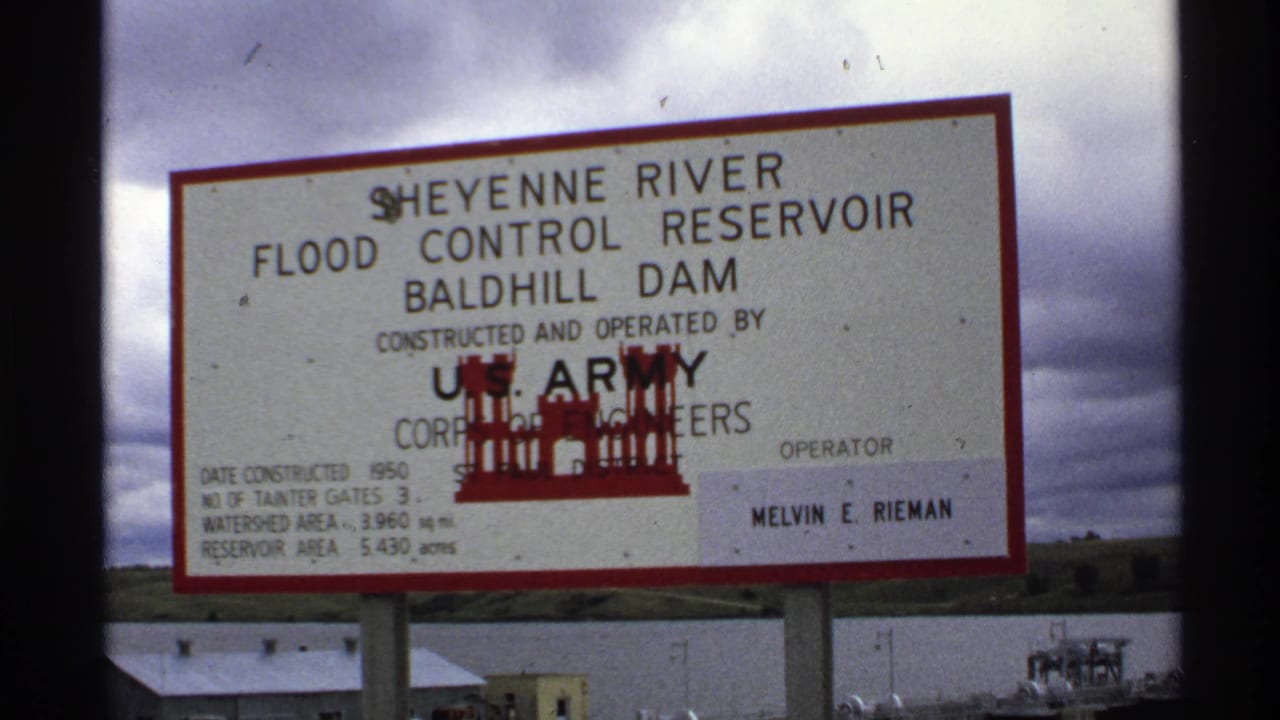 Red-bordered Sheyenne River Flood Control Reservoir sign in front of dam facilities and cloudy sky.