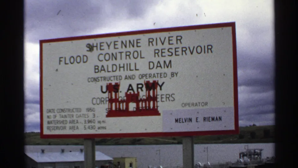 1972 North Dakota 8mm frame showing the Baldhill Dam reservoir sign with U.S. Army Corps of Engineers text and structures below.