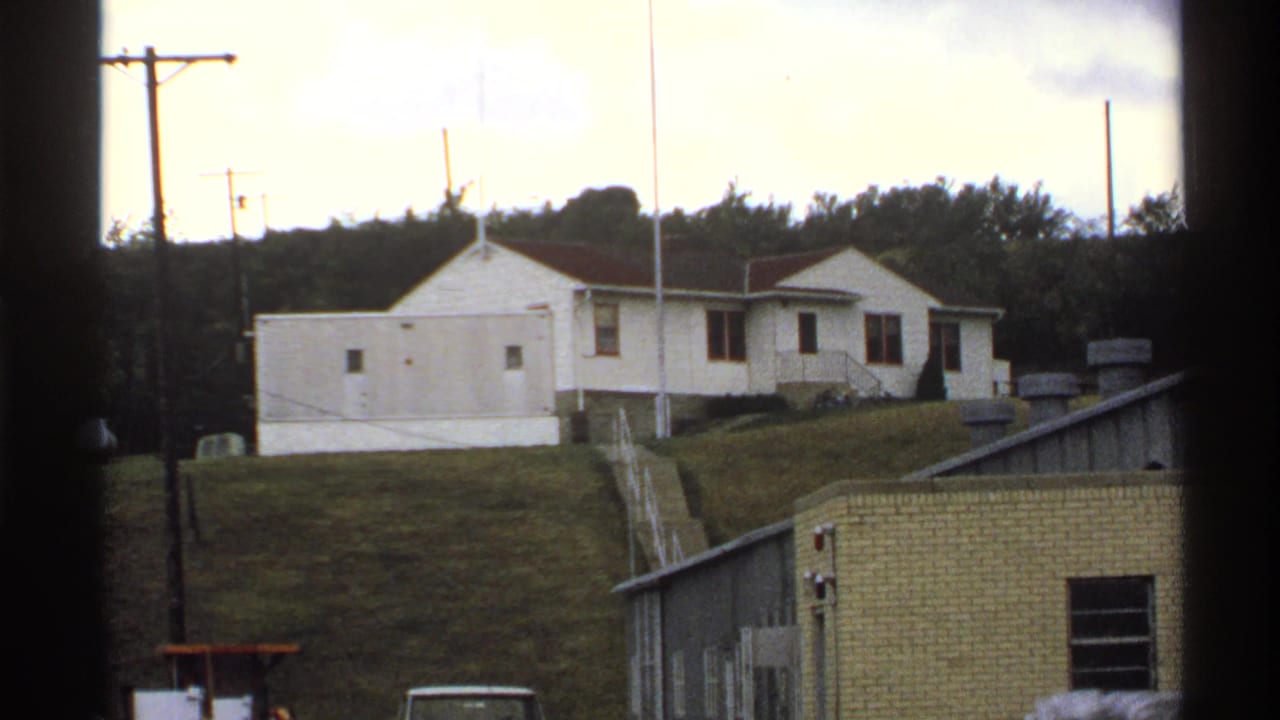 White building on a grassy slope with utility poles and low structures nearby.