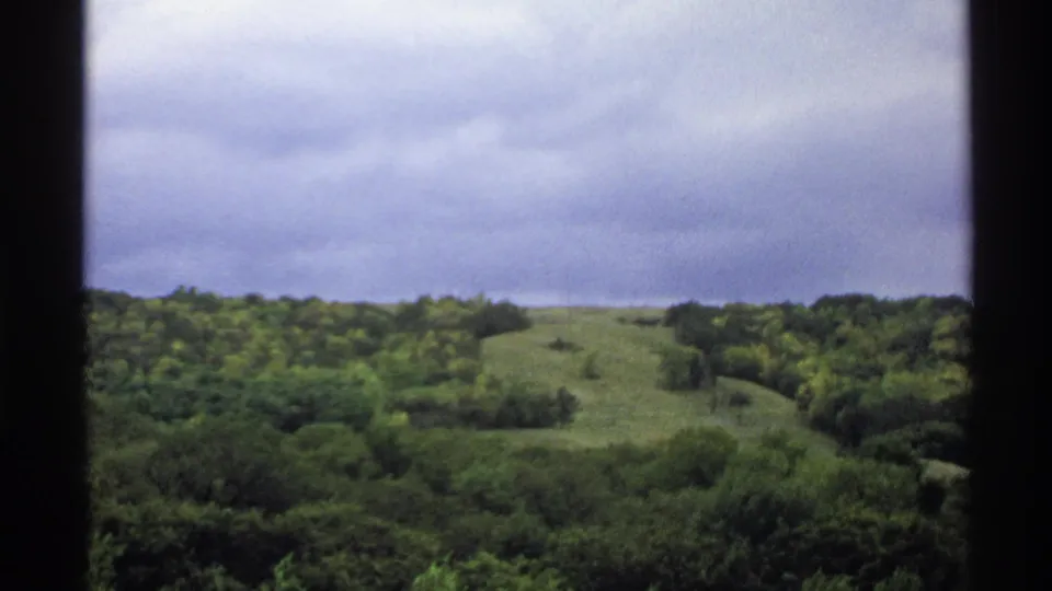 1972 North Dakota 8mm frame showing rolling wooded terrain and low gray clouds from a home-movie viewpoint.