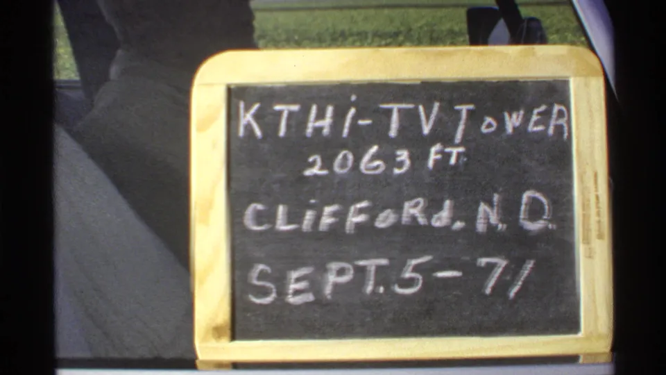 Handwritten 1972 Clifford, North Dakota KTHI-TV tower sign fills the frame, with vehicle interior edges and a partial figure nearby.