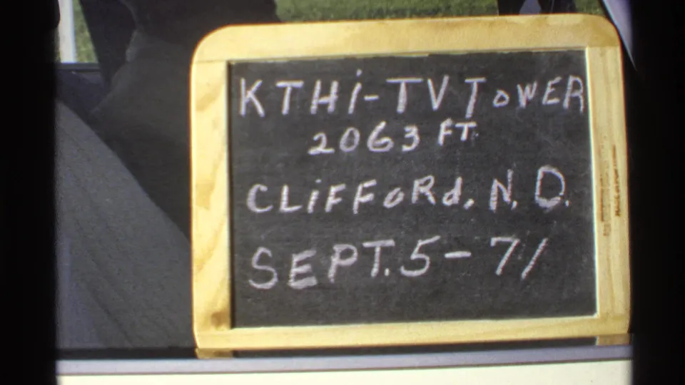 Chalkboard sign for the KTHI-TV Tower near Clifford, North Dakota, seen through dark vehicle-window edges in a 1972 home-movie frame.