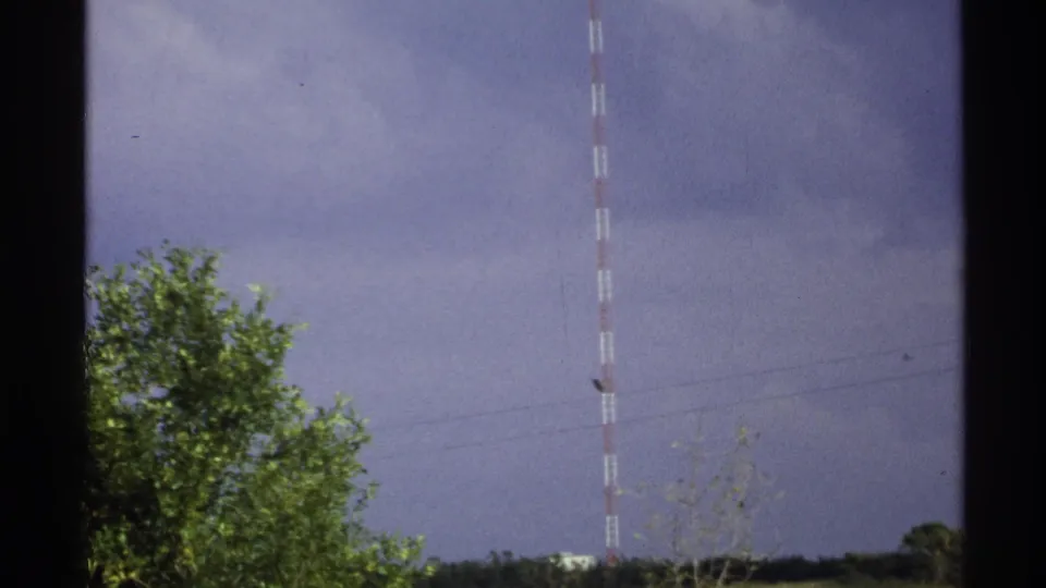 1972 North Dakota 8mm frame showing a red-and-white transmission mast above green trees and a low rural horizon.