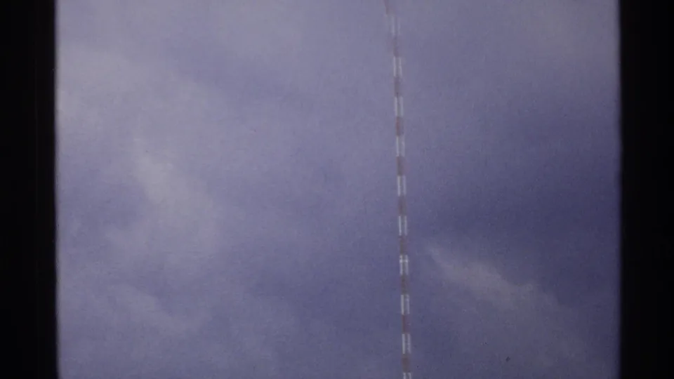 Closer 8mm view of the striped transmission mast in North Dakota, with most of the frame filled by gray-blue cloud cover.