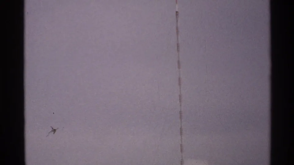 A central dark tower or antenna element crosses a pale 1972 North Dakota sky, with faint lines and visible 8mm grain.
