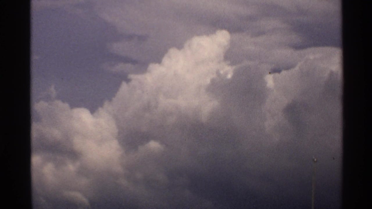 1972 North Dakota 8mm frame showing voluminous clouds in a muted sky, with film borders and grain visible.