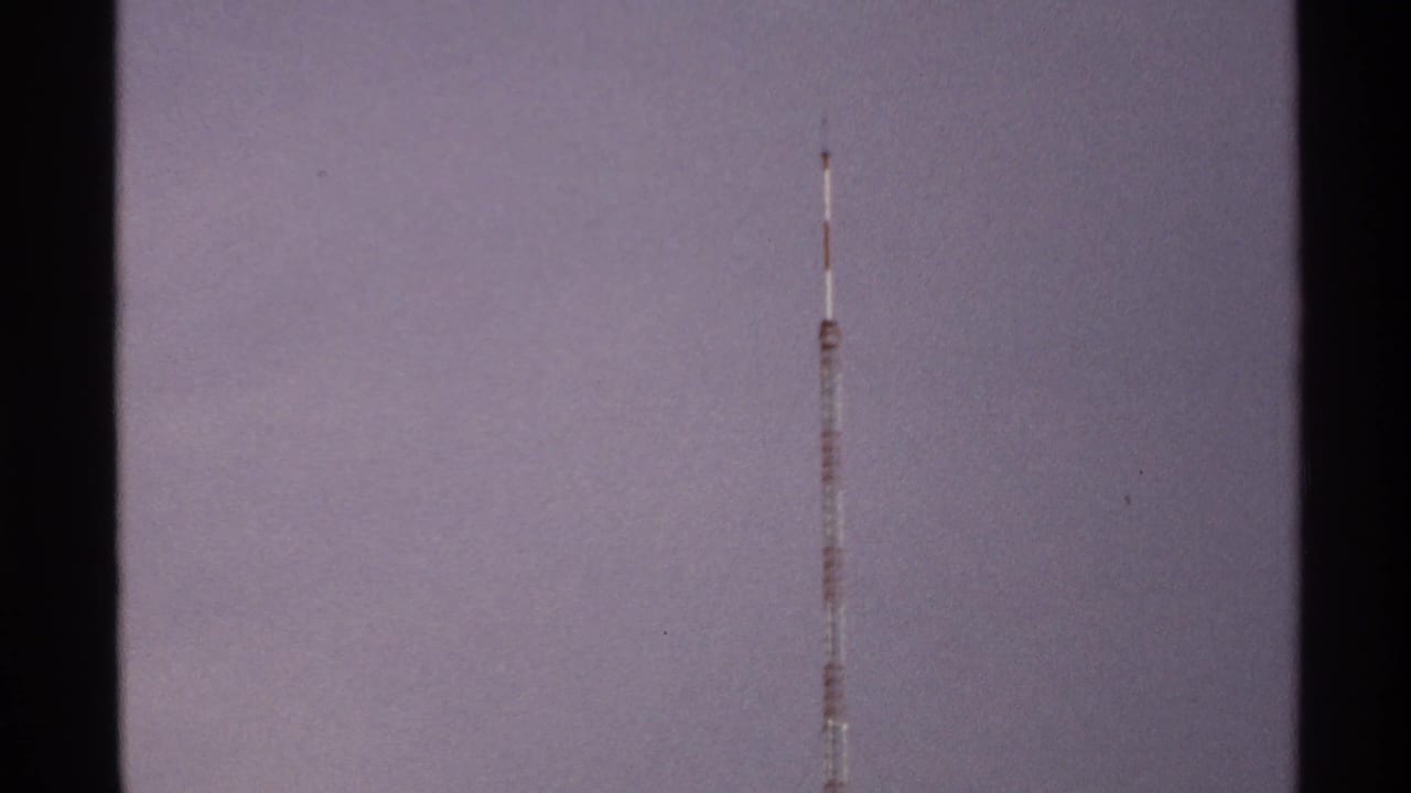 A slender red-and-white communication tower stands high against the hazy North Dakota sky in 1972 home-movie footage.