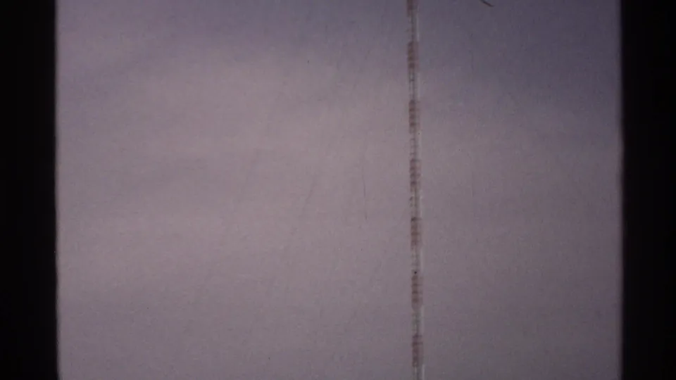 A tall communication tower stretches through a hazy, clouded North Dakota sky in this 1972 8mm frame.