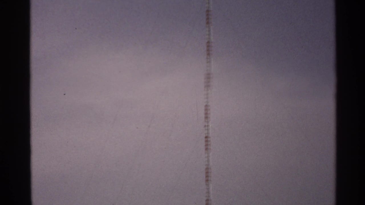 Pale sky with a narrow red-and-white antenna line and dark film-edge bars.