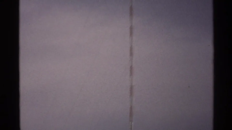 North Dakota 1972 home-movie frame with the antenna faintly visible against a washed, grainy sky.