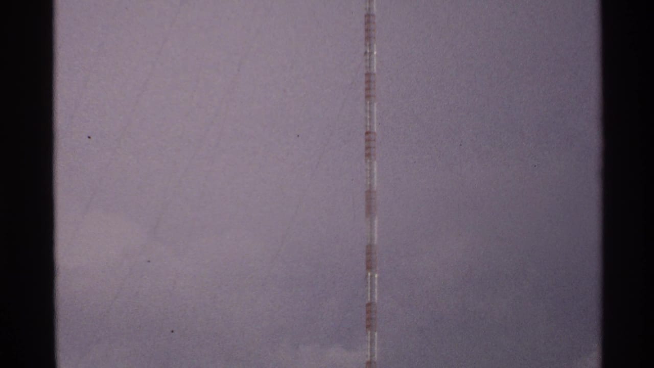 A tall red and white striped tower rises into a cloudy North Dakota sky in 1972 8mm home-movie footage.