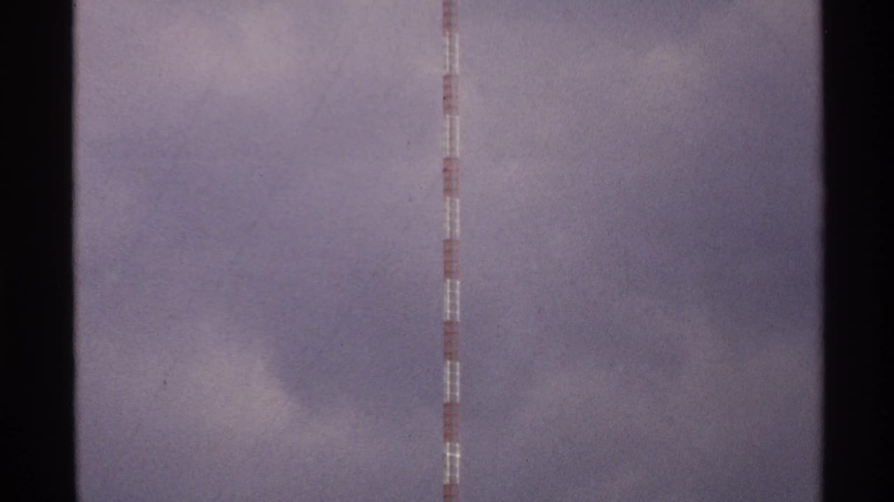 The camera holds on the upper section of a red and white tower against soft clouds in 1972 North Dakota footage.