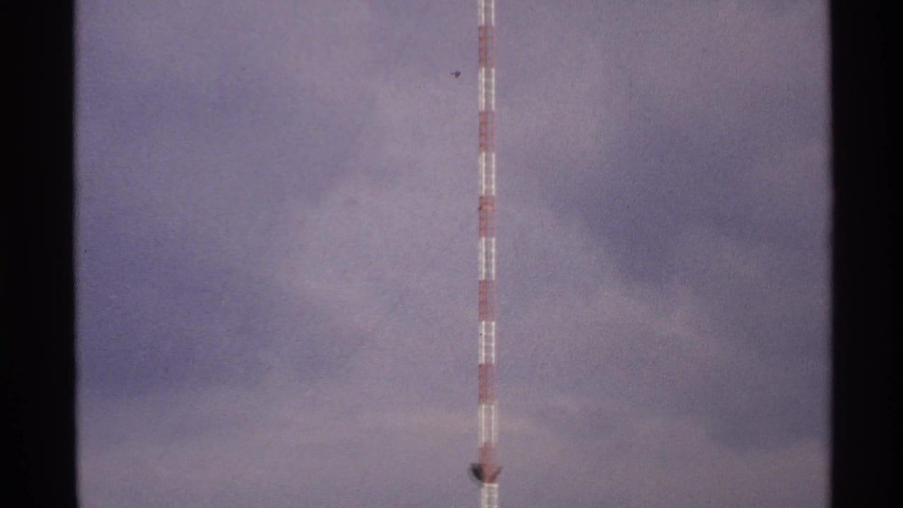 Red-and-white tower rising into cloudy sky with dark film borders.
