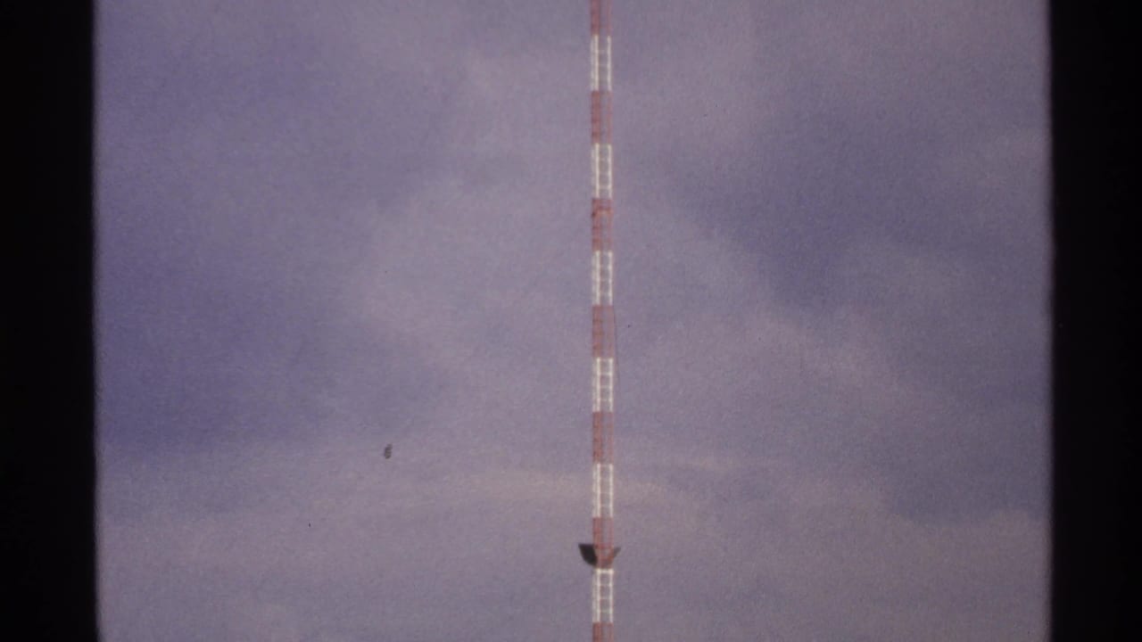 Striped communications tower in a cloudy North Dakota sky, recorded on faded 8mm home-movie film.