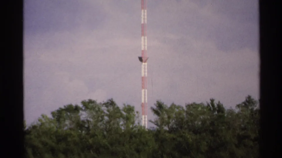 1972 8mm view of a red-and-white tower extending above green trees in rural North Dakota.
