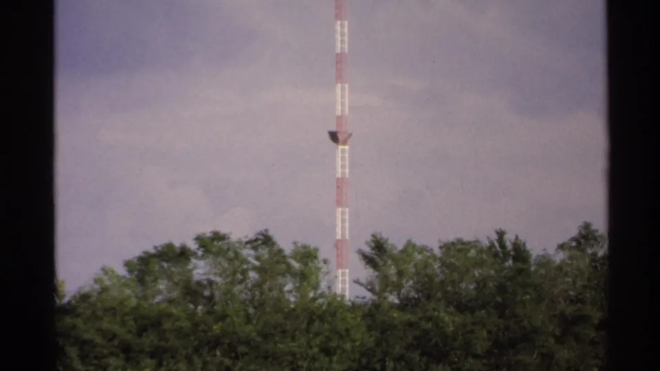 North Dakota home-movie frame showing the tower behind treetops, with muted 8mm color and visible grain.