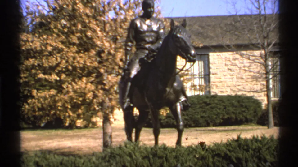 1972 Saint Louis 8mm frame showing the bronze equestrian statue partly cropped, with hedges, lawn, and fall trees nearby.