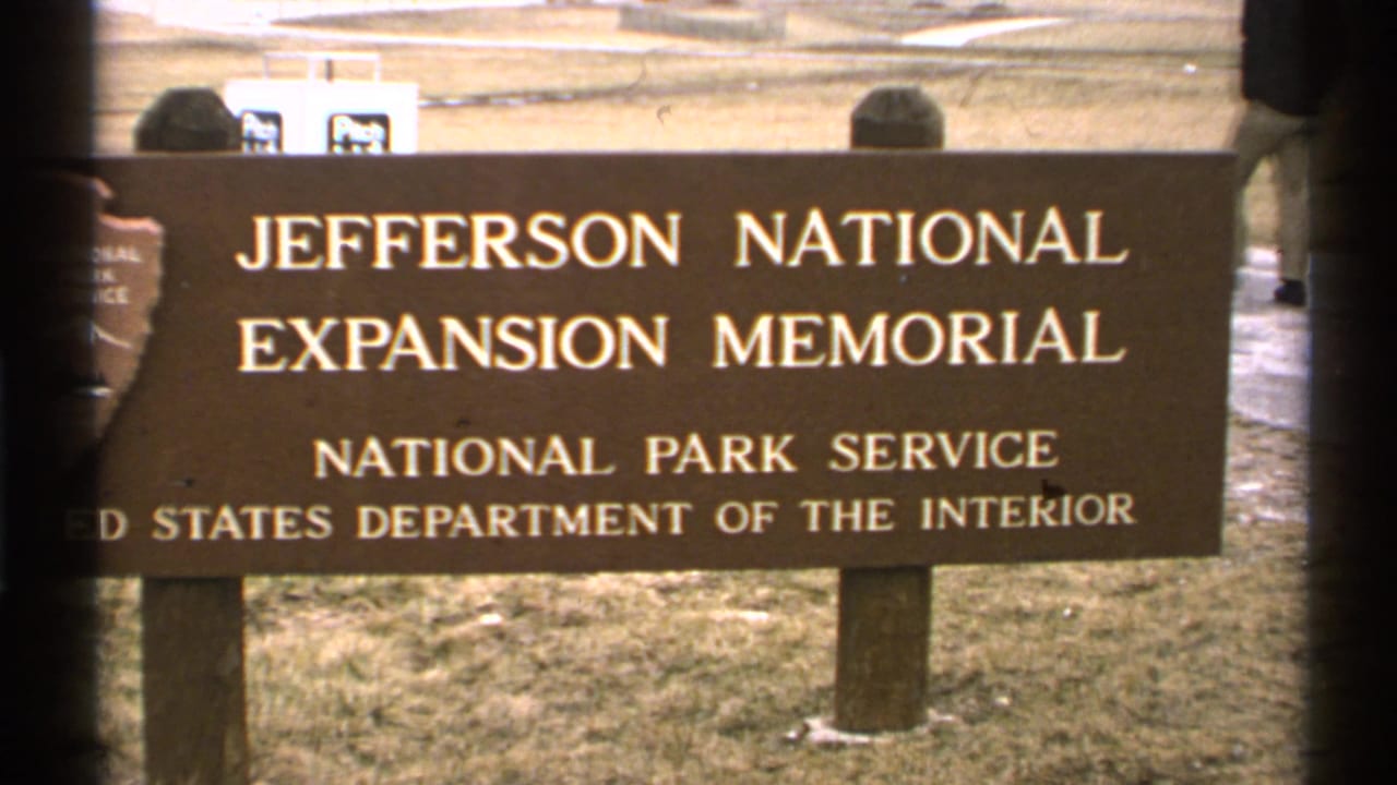 Jefferson National Expansion Memorial sign beside a grassy area, partly framed by dark window edges.