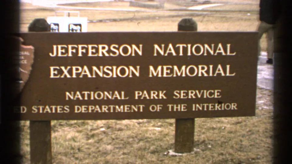 1972 Saint Louis 8mm frame showing the Jefferson National Expansion Memorial National Park Service sign with a passerby partly visible behind it.