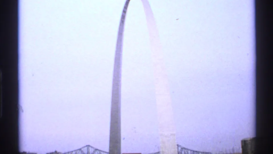 1972 Saint Louis 8mm frame looking up at the Gateway Arch, with a bridge or structure low in the frame and dark window-like edges.
