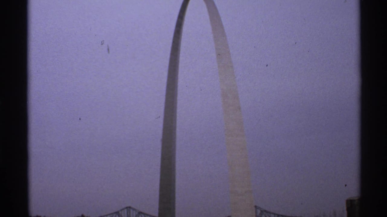 Gateway Arch centered in a distant view with cloudy sky and dark film border.